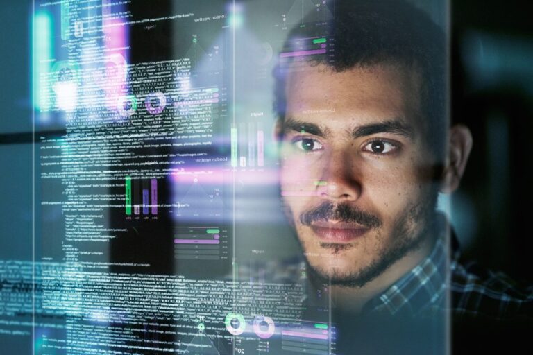 jovem pardo de bigode vê em vidro reflexo de um código em desenvolvimento para ilustrar artigo sobre a profissão de engenheiro de software
