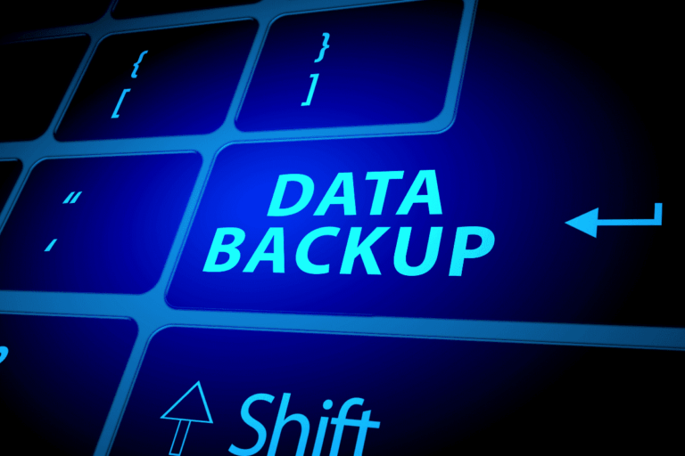a imagem que ilustra artigo sobre integridade de dados com backups mostra um teclado de computador com destaque para a tecla Shift e a seta de retorno (Enter) à direita. No centro da imagem, há um destaque em azul brilhante com o texto "DATA BACKUP" (Backup de Dados). As teclas são iluminadas com uma luz azul, dando um efeito moderno e tecnológico.