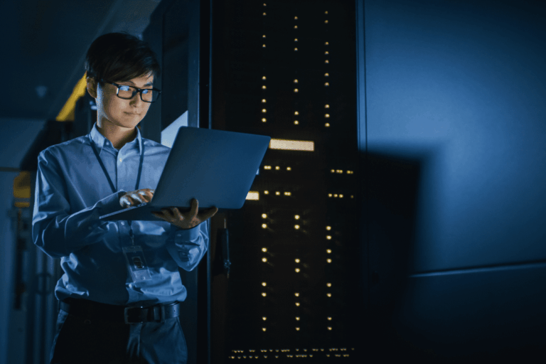 ilustrando artigo sobre sistemas operacionais para mainframes, vemos na foto um jovem de origem asiática segurando um computador em um ambiente de servidores