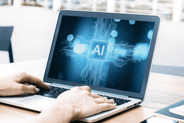 pessoa digitando em laptop que exibe uma tela com o símbolo 'AI' no centro, representando a inteligência artificial nas empresas. Linhas e circuitos digitais em azul claro saem do símbolo, sugerindo o processamento de dados e a interconectividade da tecnologia. O cenário sugere um ambiente de trabalho moderno.