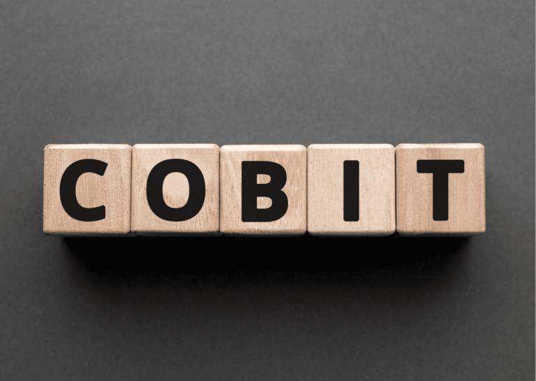 Exemplificando o que é COBIT, estão, sobre fundo cinza, dispostos cinco cubos de madeira clara, cada um com uma letra em preto, formando a palavra COBIT.