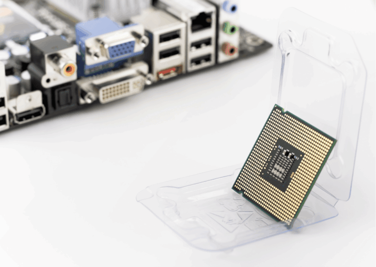 Exemplificando a evolução dos processadores, estão sobre uma superfície branca, ao fundo, portas e entradas de computadores e, em destaque, um chip de processador verde com placa dourada disposto sobre uma superfície de apoio transparente que o deixa em pé e levemente inclinado para trás.